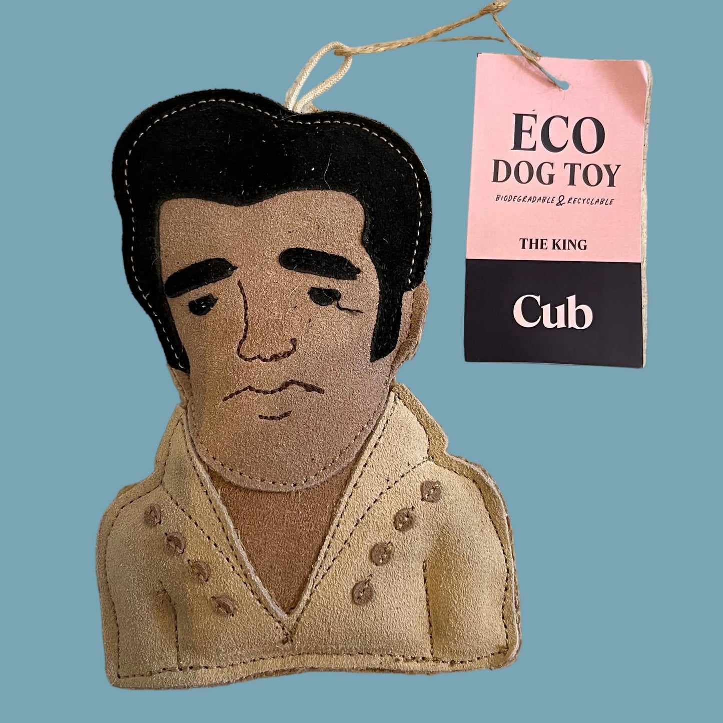 A handmade felt dog toy shaped like Elvis Presley's bust, featuring black hair and a beige jacket, with a pink and black hangtag reading 'ECO DOG TOY' and 'Cub'.